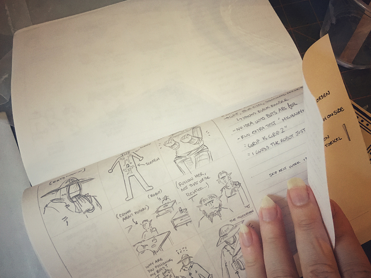  A hand holds open a textblock to a sketchbook page, the fingers lifting up a smaller page of notes that have been stapled to the edge of the page.