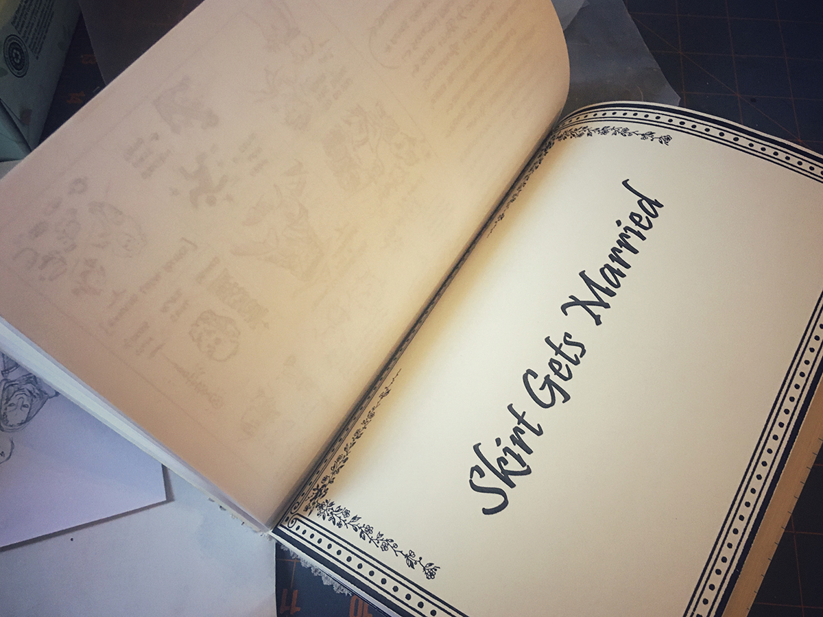 A textblock opened up, laying flat, the pages are open to a section divider with a tidy black and white border design and, in a simple script, "Skirt Gets Married."