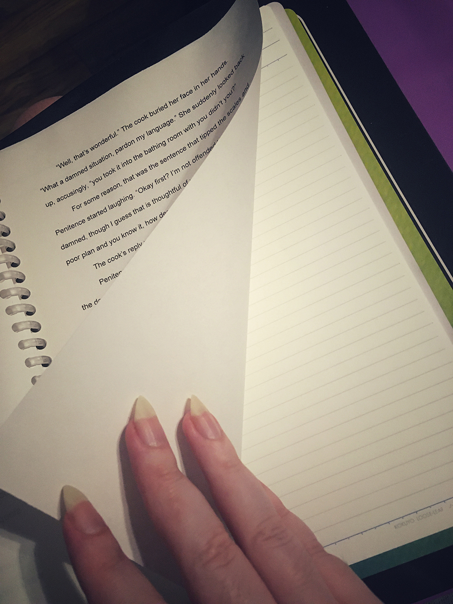 A hand flips back a page of a B5 notebook. The sheet that is partly turned back has printed text on it, but the sheets behind it are lined and blank.