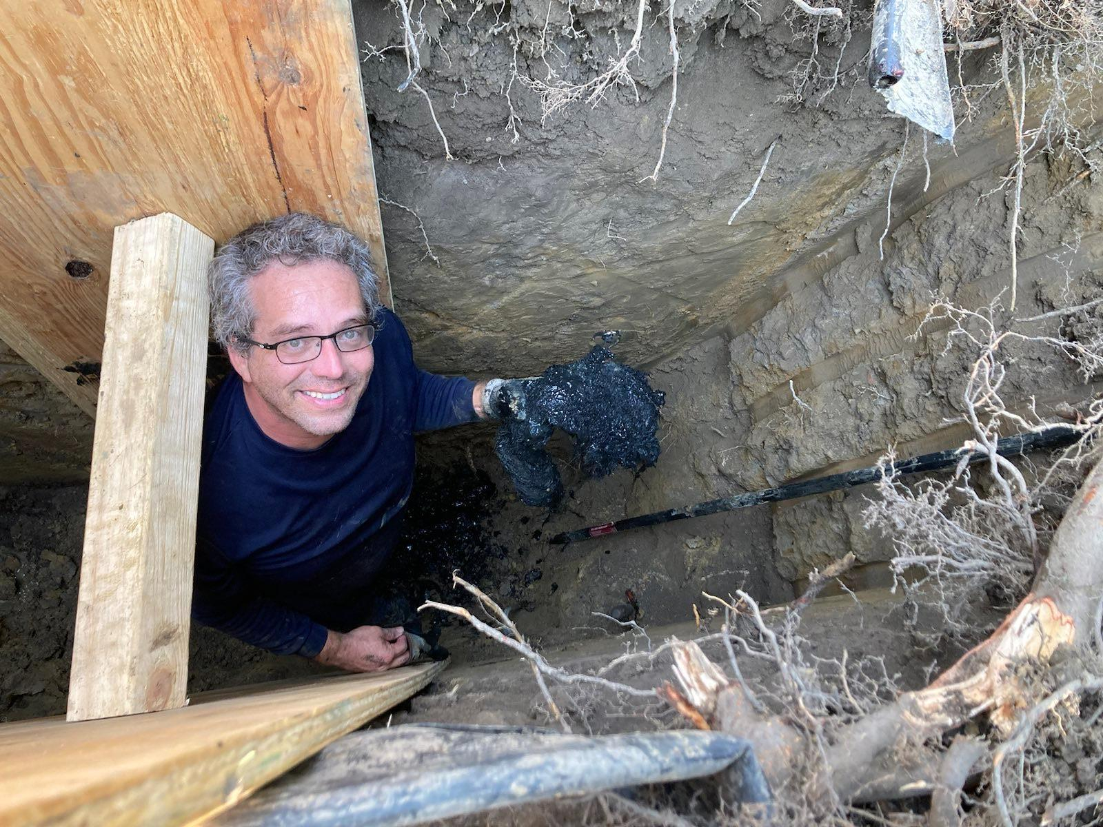 Cristobal looking up and smiling from the trench while repairing a damaged sewer line