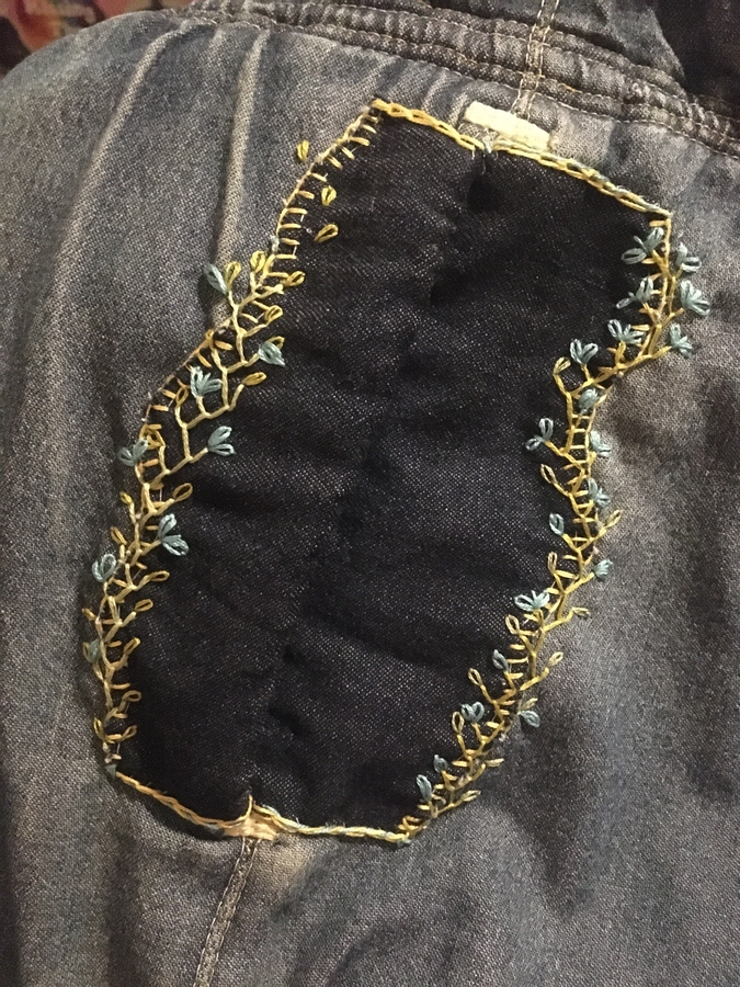 The same pocket, patched with more lightweight denim that covers the worn edges and extends onto the coat in a scalloped pattern, the edges covered with simple embroidered vines and flowers.