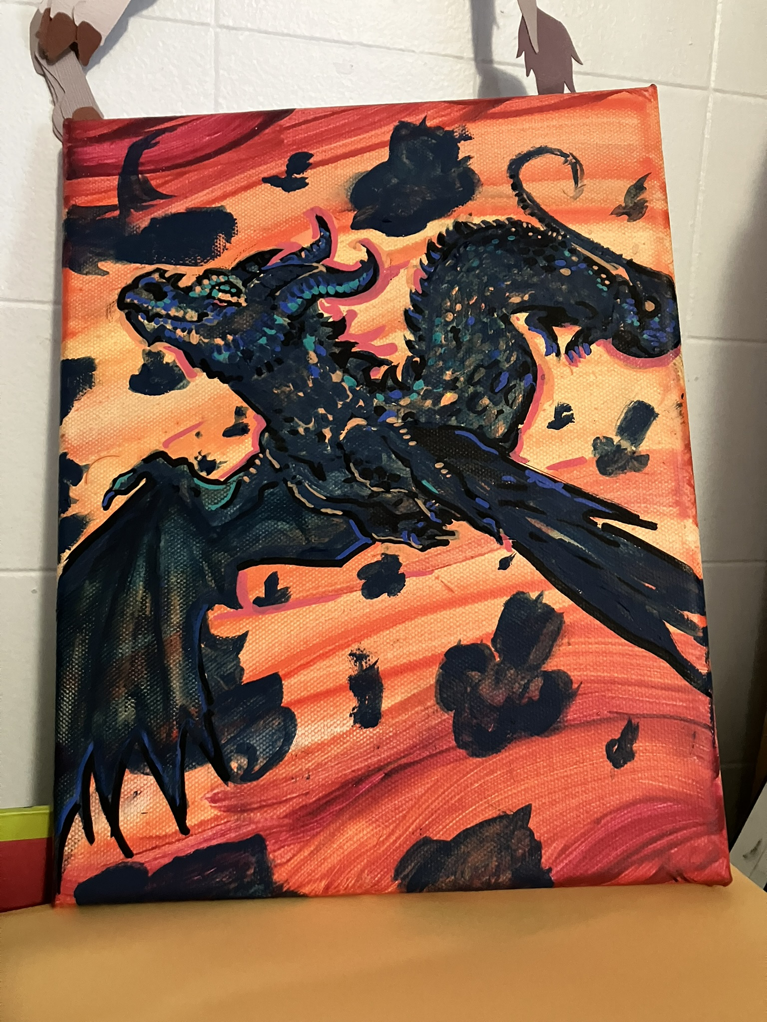 a painted larger canvas of a black scaled dragon flying through a bright orange and red sky amid a series of airships