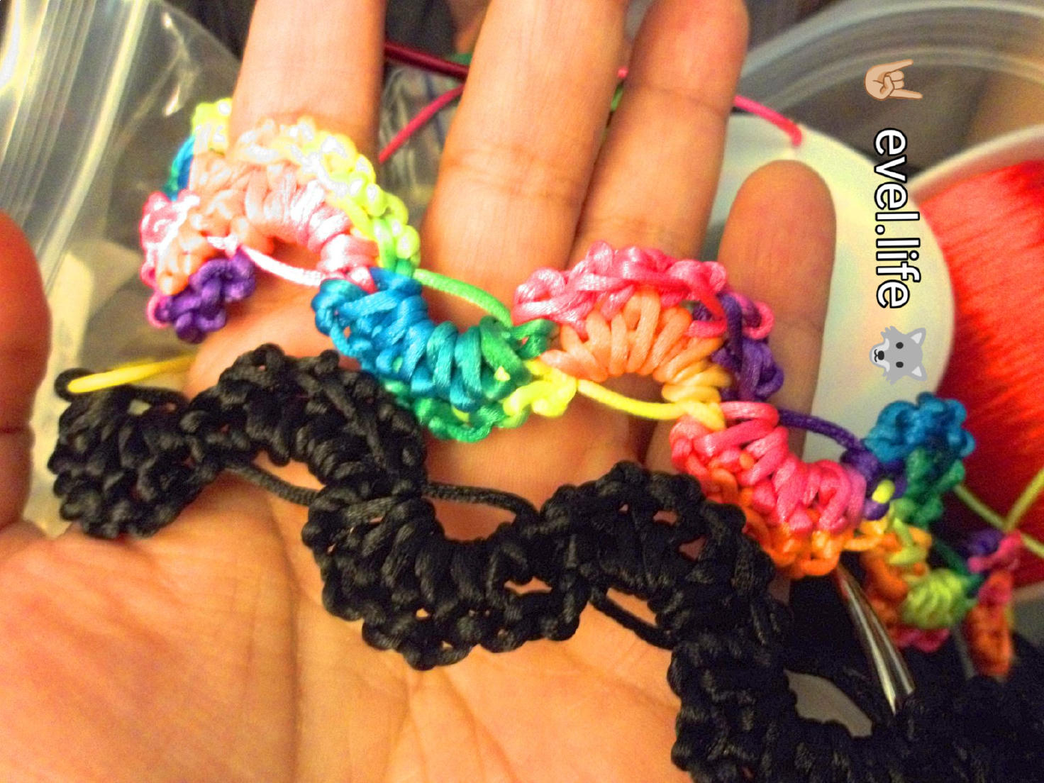 a brown hand holding crocheted bracelets. the bracelets are wavy with a lot of texture! one is black and one is rainbow.