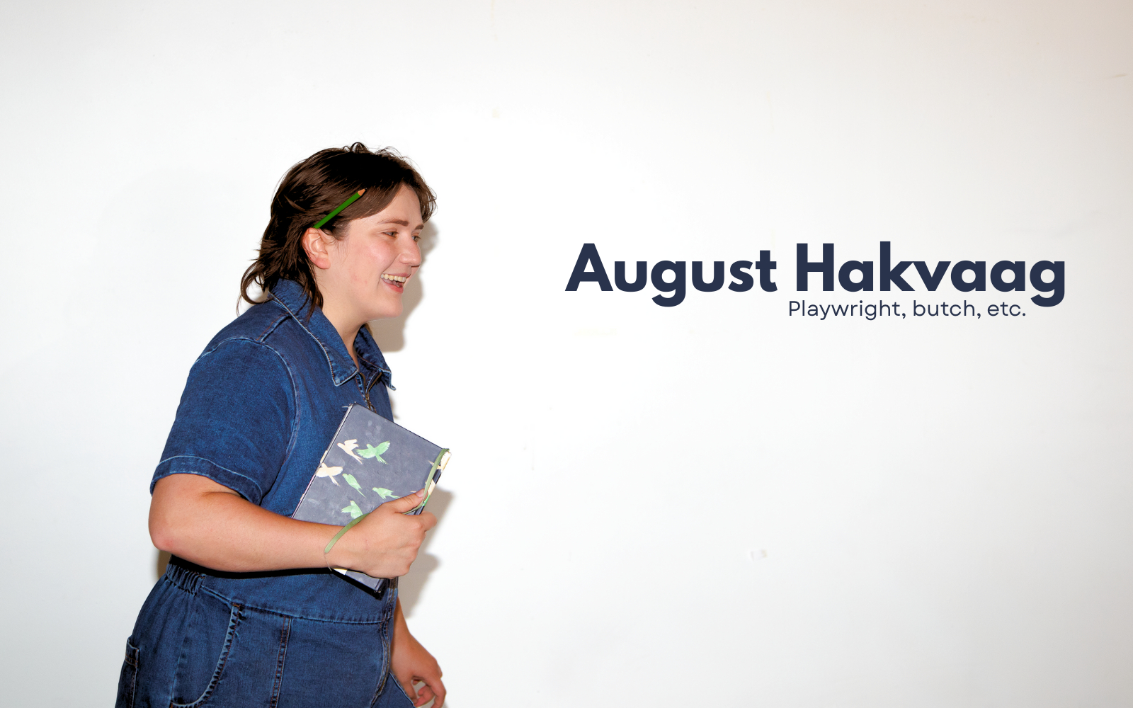 A picture of a smiling August Hakvaag wearing a blue denim jumpsuit and holding a notebook. Text reads: August Hakvaag. Playwright, butch, etc.